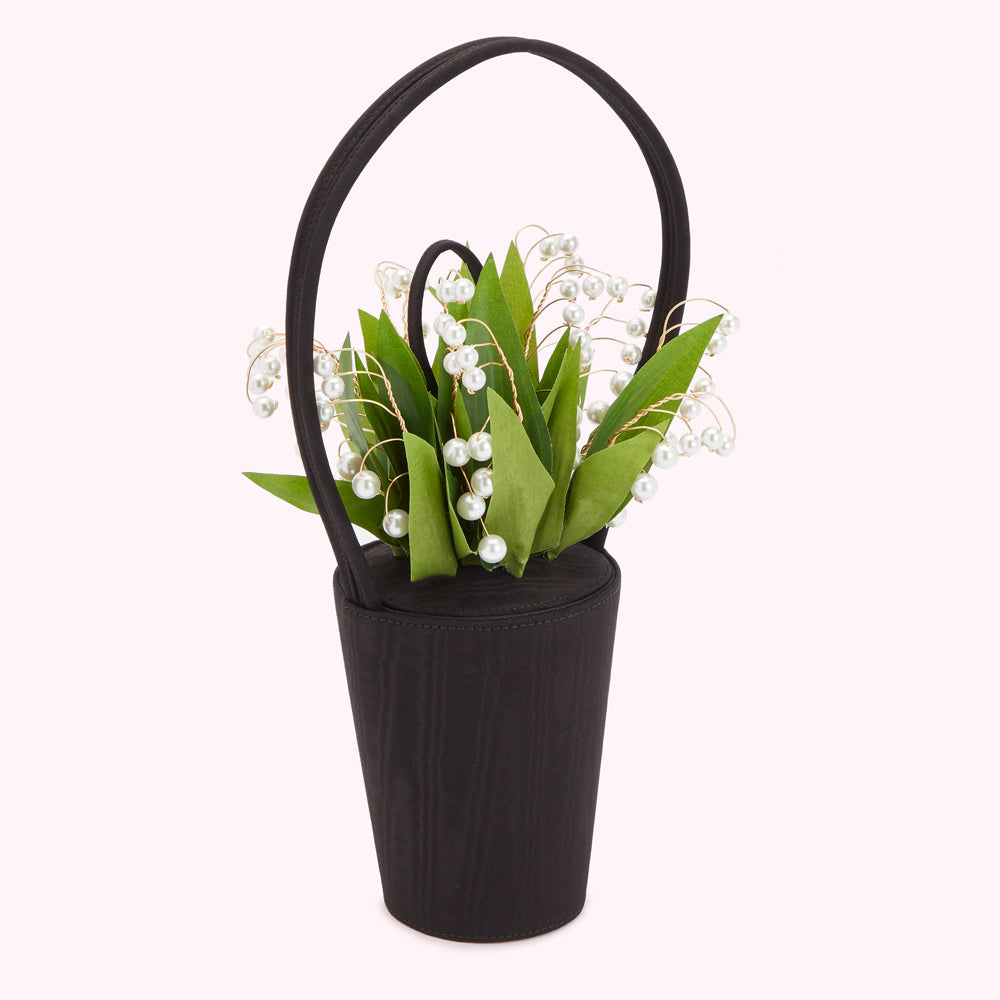 Black cylindrical handbag with a top handle adorned with a bouquet of lily of the valley and pearls.
