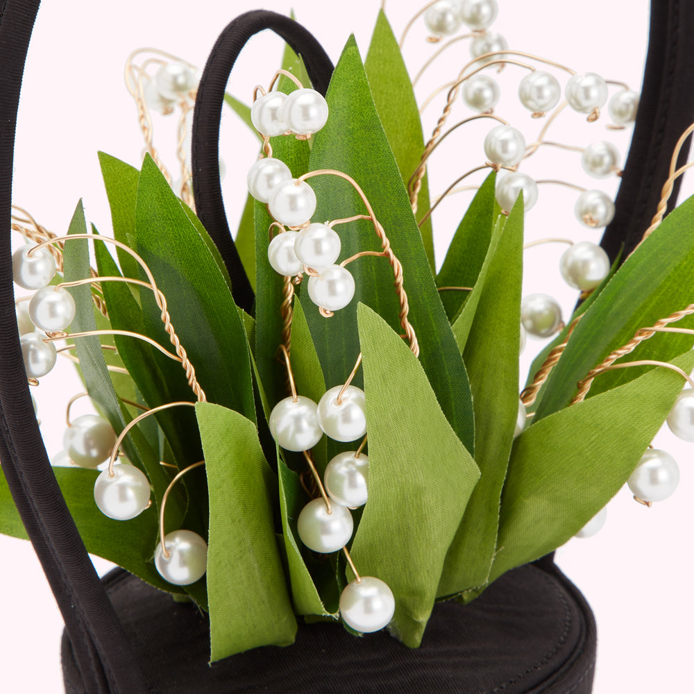 Close-up of a black handbag adorned with artificial lily of the valley flowers and pearl accents.