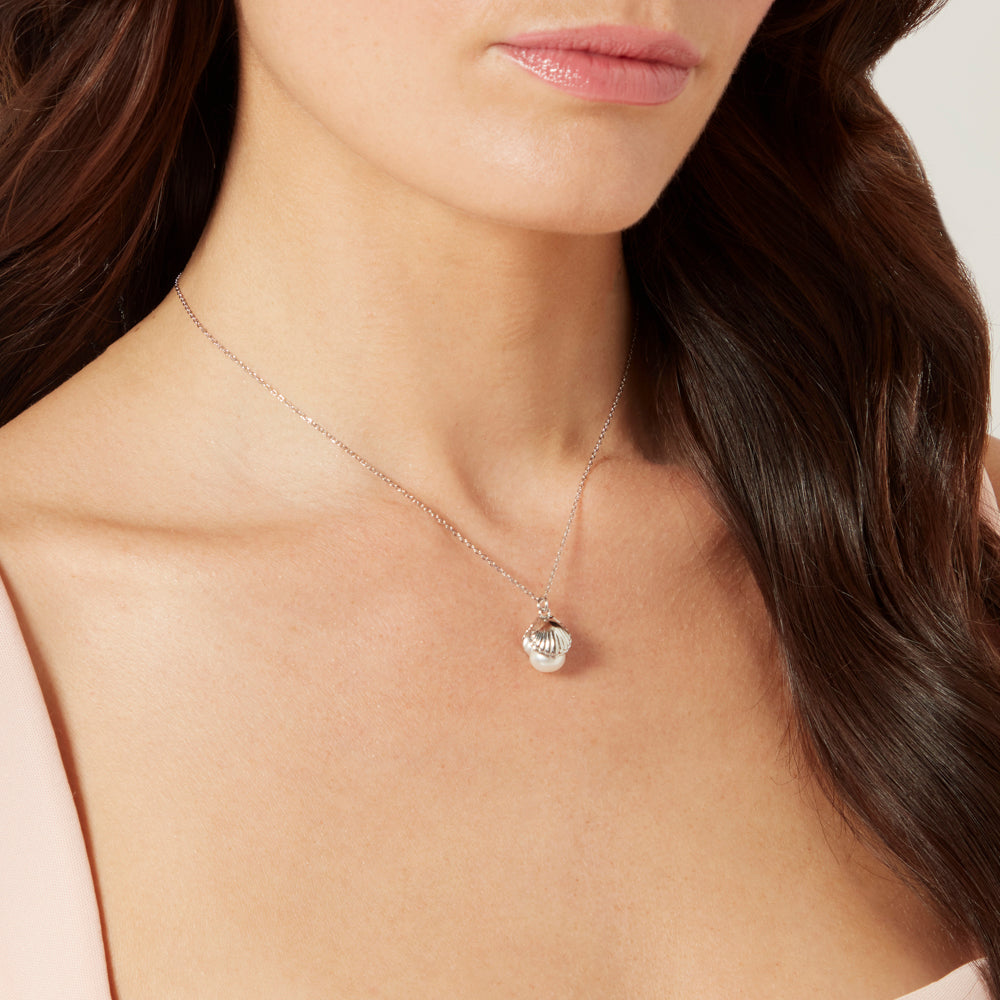 Model with dark hair wearing a sterling silver shell shaped pendant with a freshwater pearl.