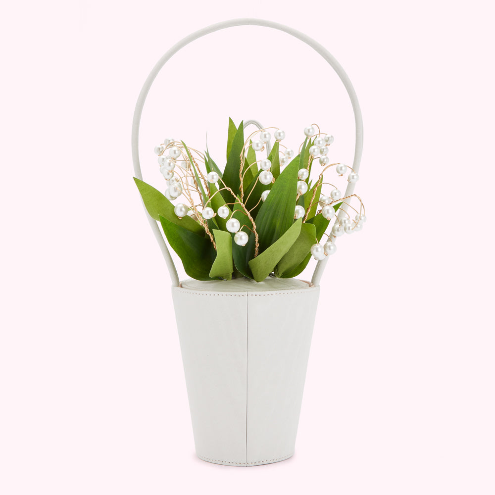 A ivory white bucket-shaped handbag with a top handle, holding a bouquet of lily of the valley adorned with pearls.
