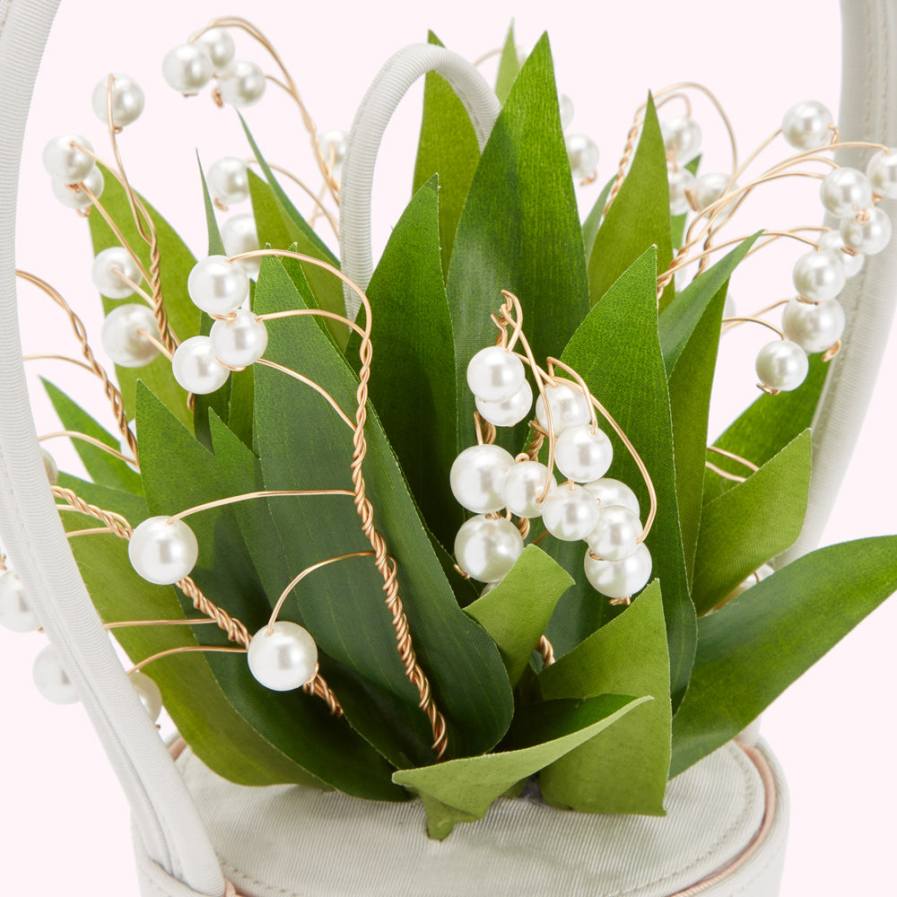 Close-up of a ivory white handbag decorated with artificial lily of the valley and pearl accents.