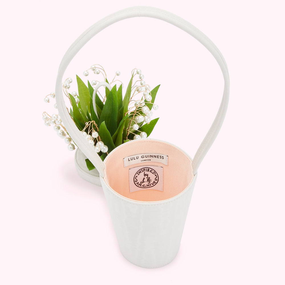 Off-white Lulu Guinness handbag shaped like a flower pot with a bouquet of lilies of the valley and pearls on top. The inside of the bag is pale pink with the brand's logo.