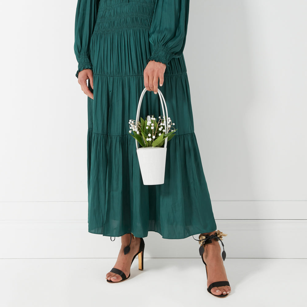 Woman in a green dress holding a small white bucket bag with lily of the valley.
