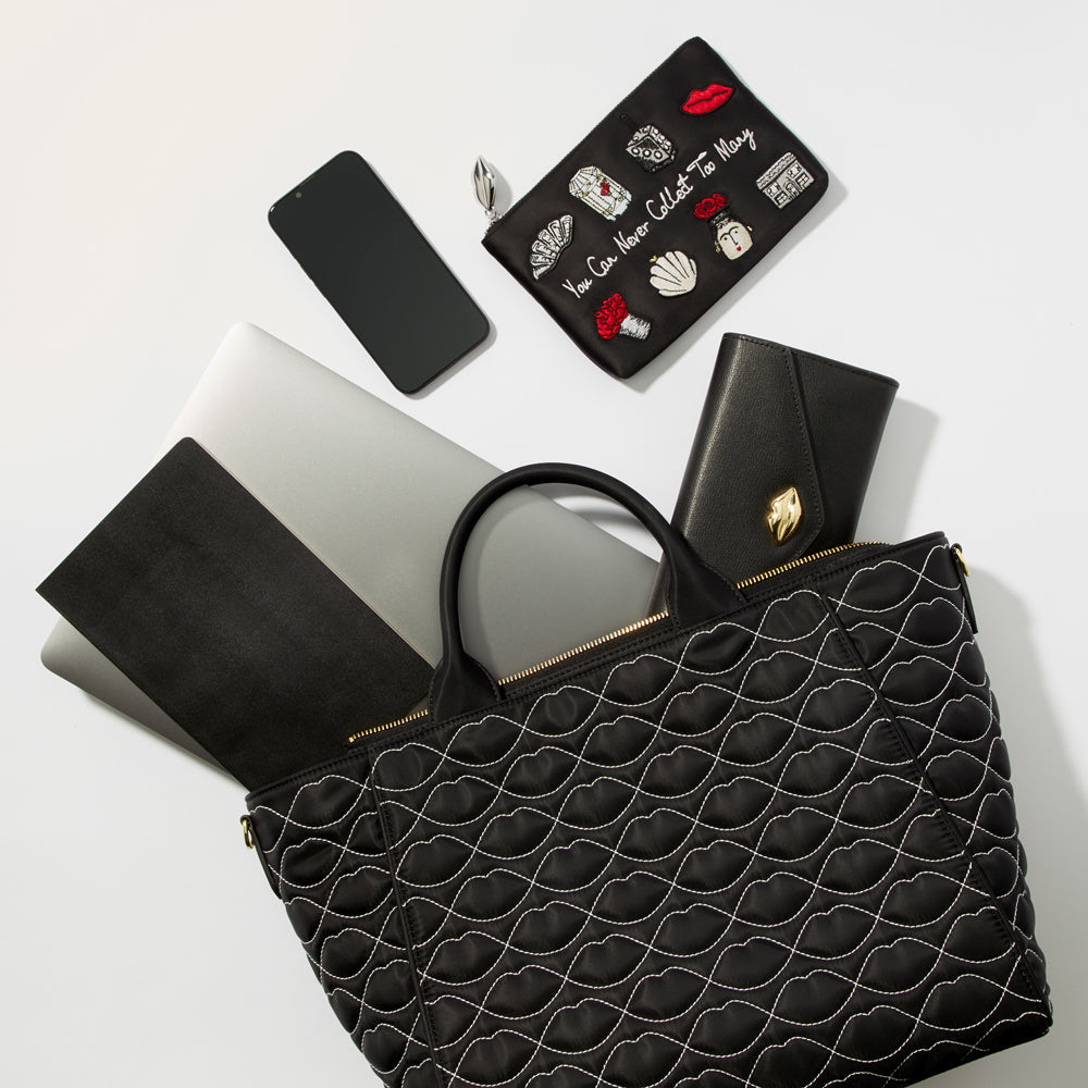 A black quilted tote bag sits on a white background with a laptop, phone, wallet, and cosmetic bag inside.
