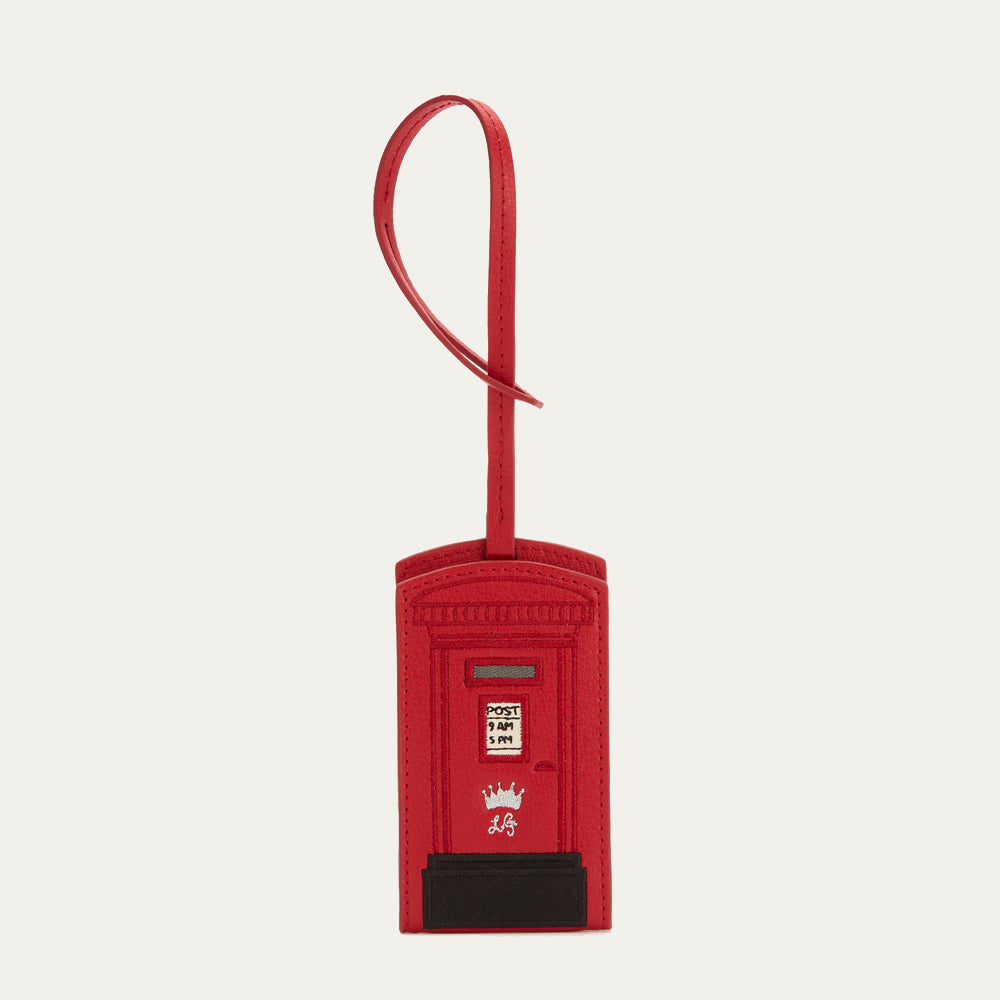 Red leather luggage tag shaped like a British postbox with a black base and a long red strap.