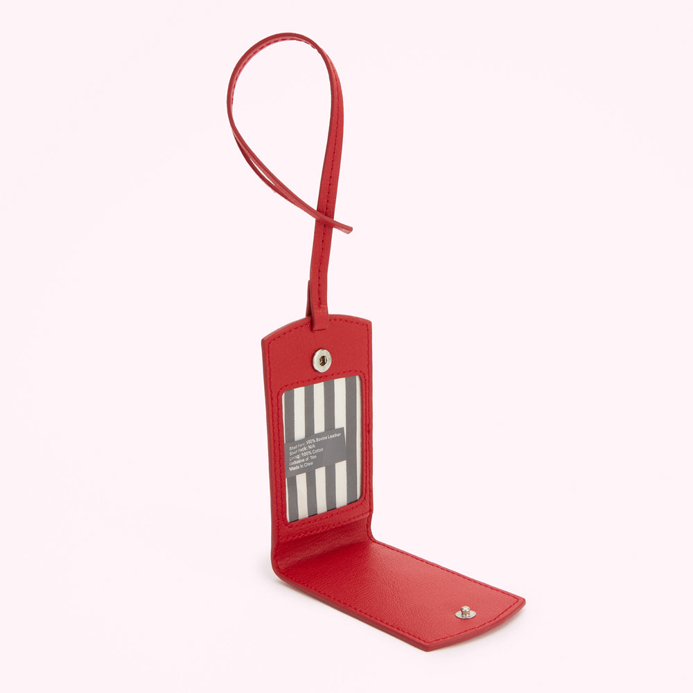 Red leather luggage tag open to reveal a black and white striped interior with product information.

