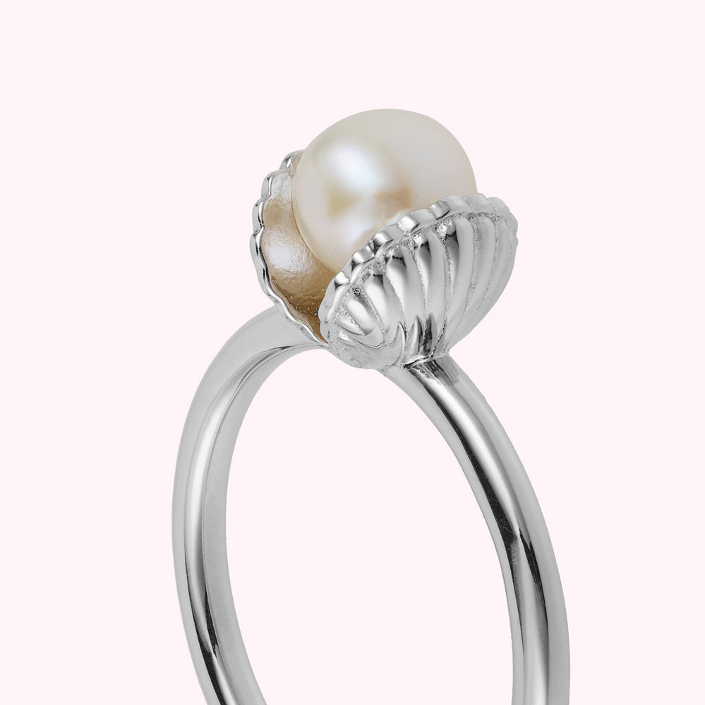 Close up detail of a sterling silver shell shaped ring with a freshwater pearl on a white background.