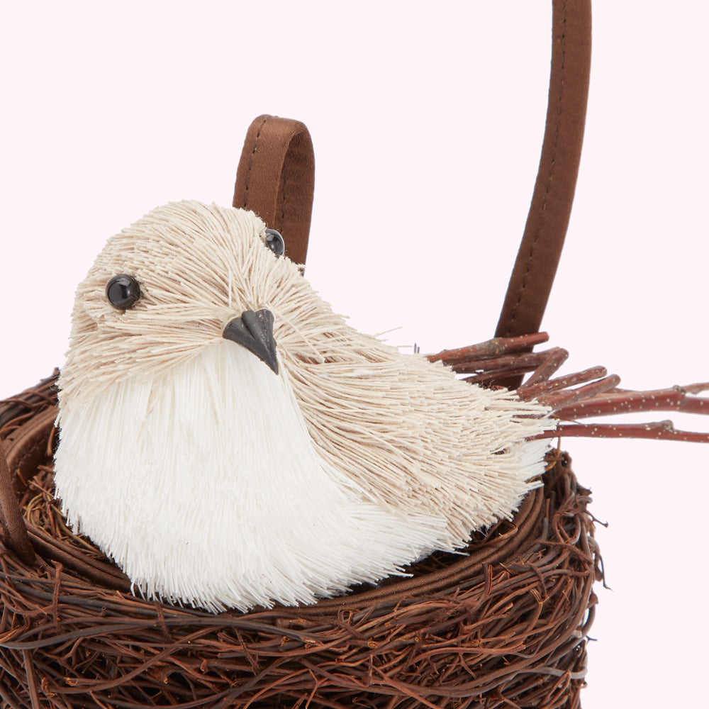 A white and beige bird sitting in a brown woven nest with a brown hangle.