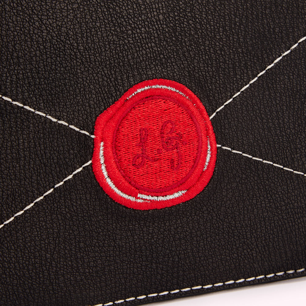 Close-up of a black leather surface with a red embroidered wax seal bearing the initials "LG".