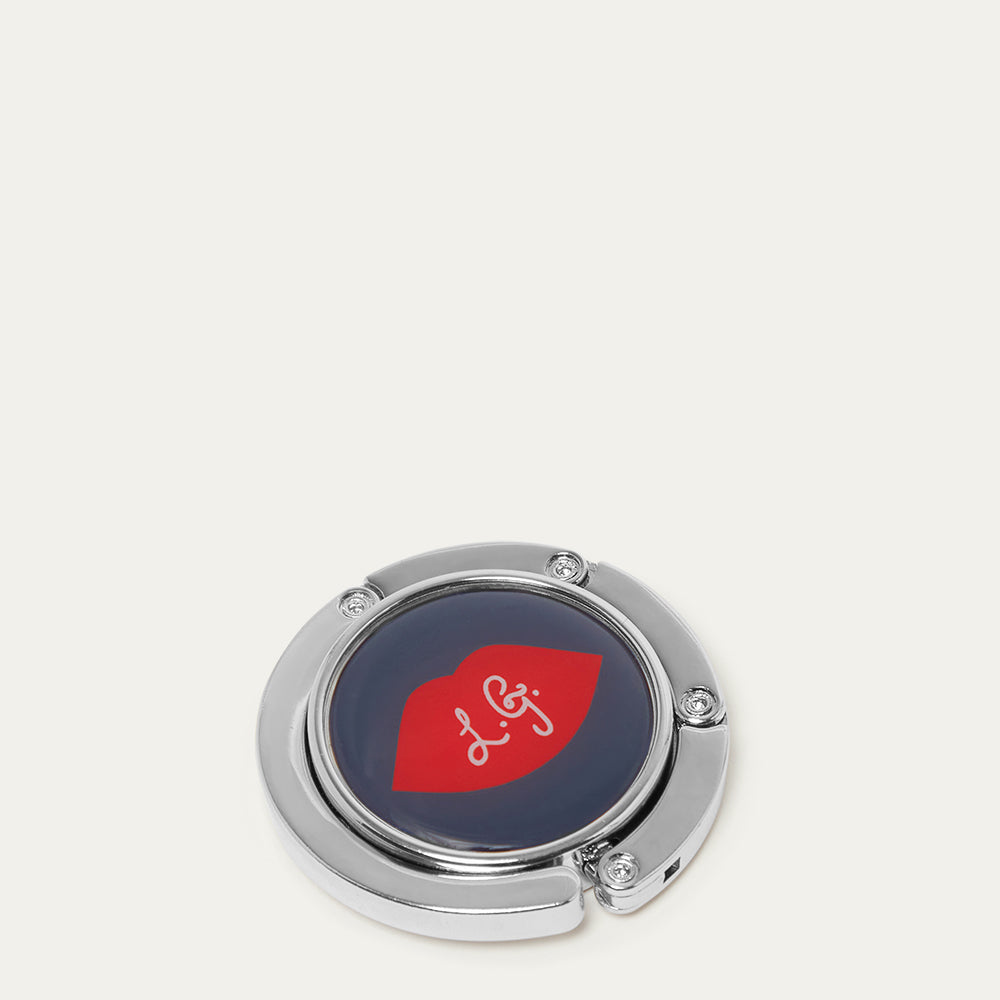 Metallic handbag hook with a red lip and white 'L.G' logo on a light gray background