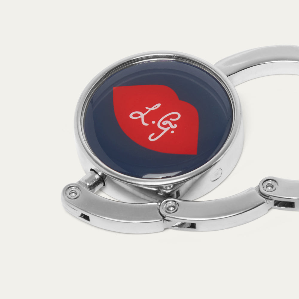 Silver handbag hook with a red lip and navy design, featuring a 'L.G' logo on a white background