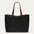 A black pebbled leather tote bag with contrasting red interior lining and red handles, shown against a light off-white background. The brand name 'LULU GUINNESS' is subtly printed in gold at the bottom center.