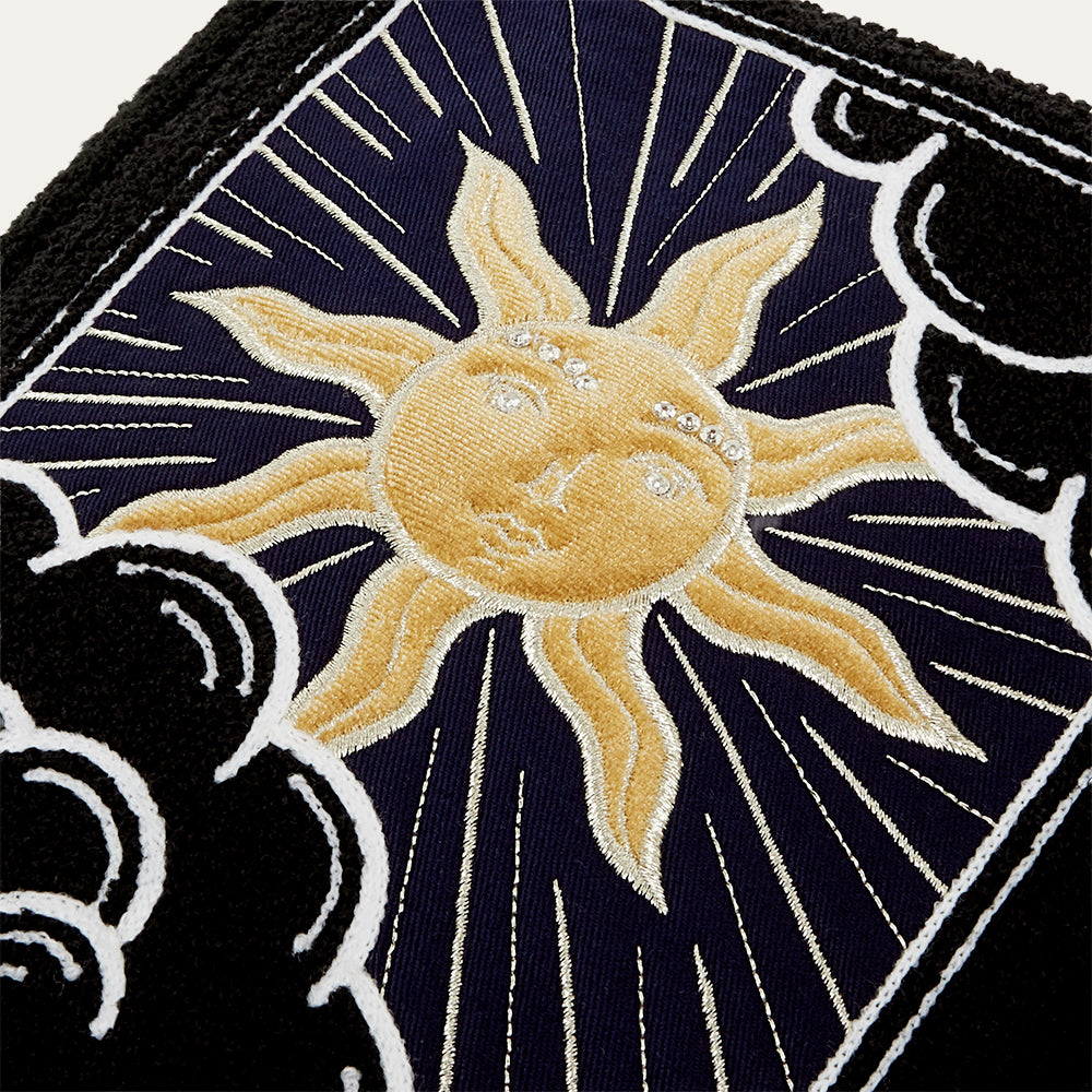 Close-up of a tote bag with a embroidered sun design on a dark background with decorative elements.