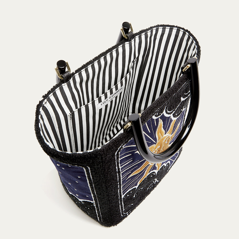Handbag with black and white striped interior and celestial design exterior on a light gray background