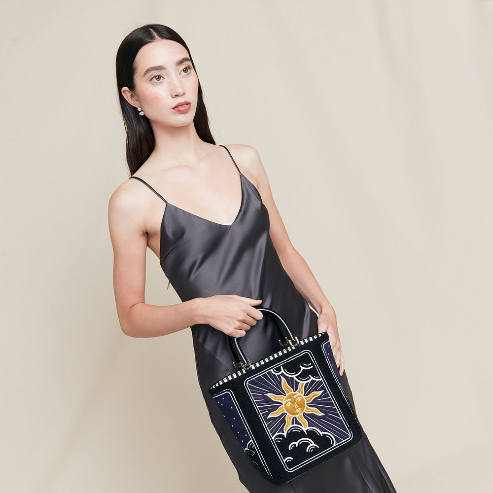 Woman holding a black handbag with a sun and moon design on a beige background