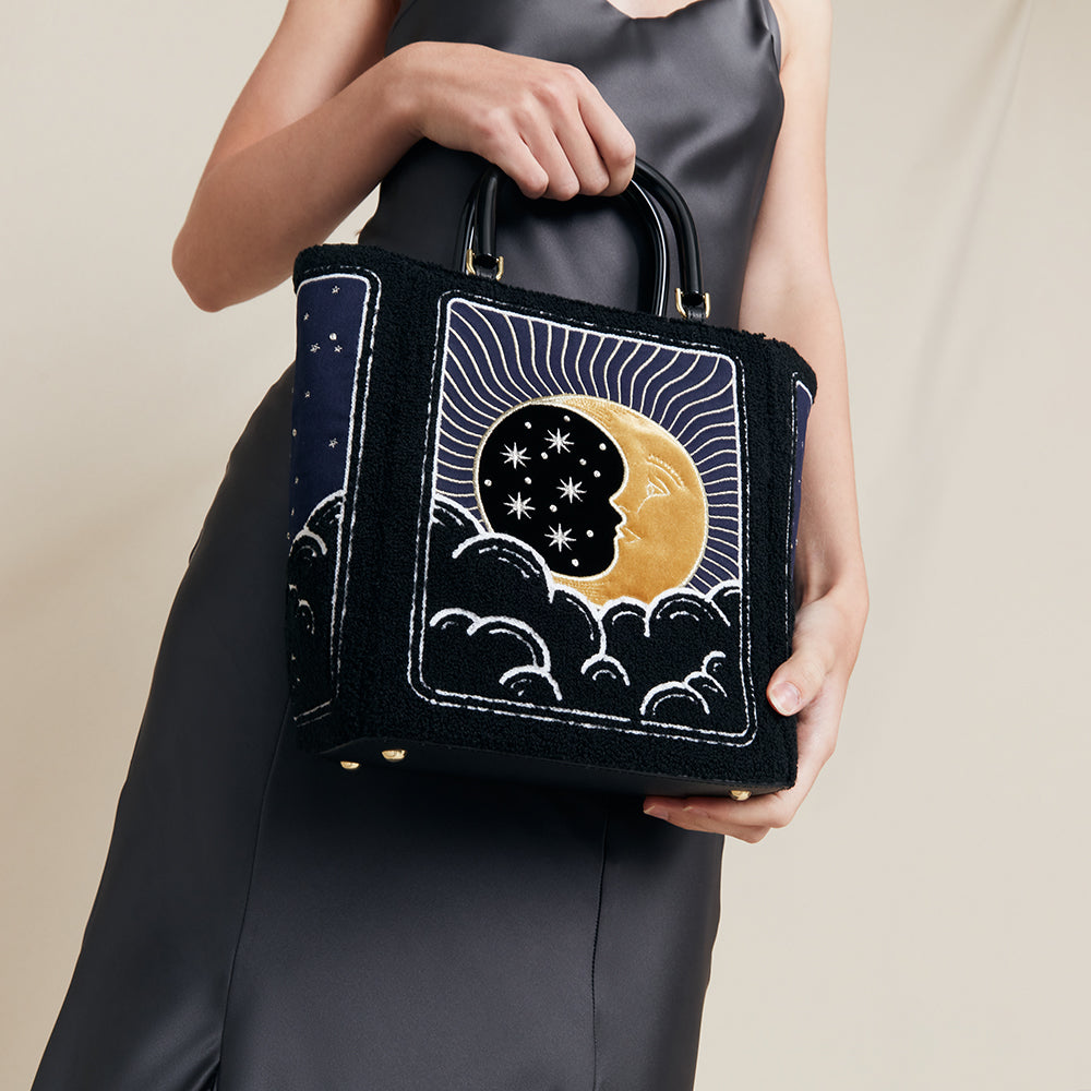 Handbag with celestial design held by a person against a neutral background