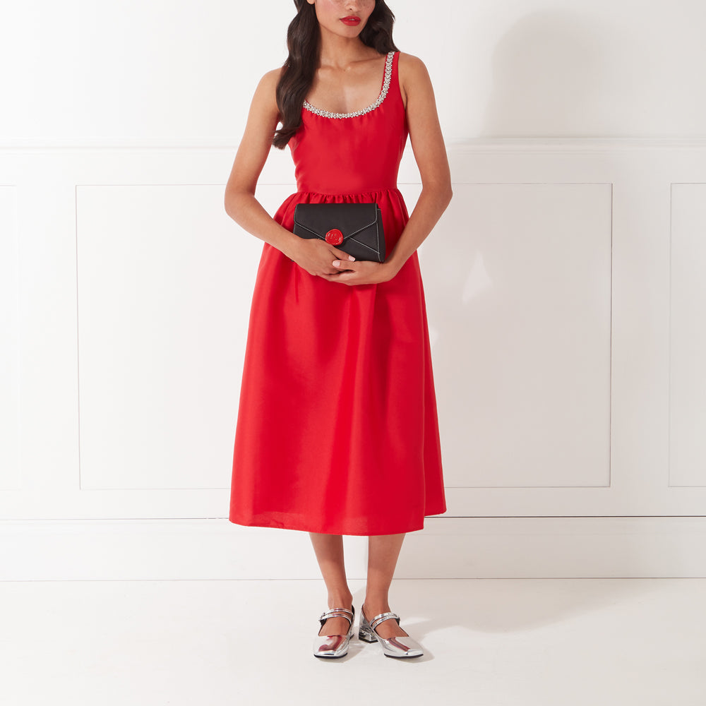 A woman in a red dress holds a black clutch.