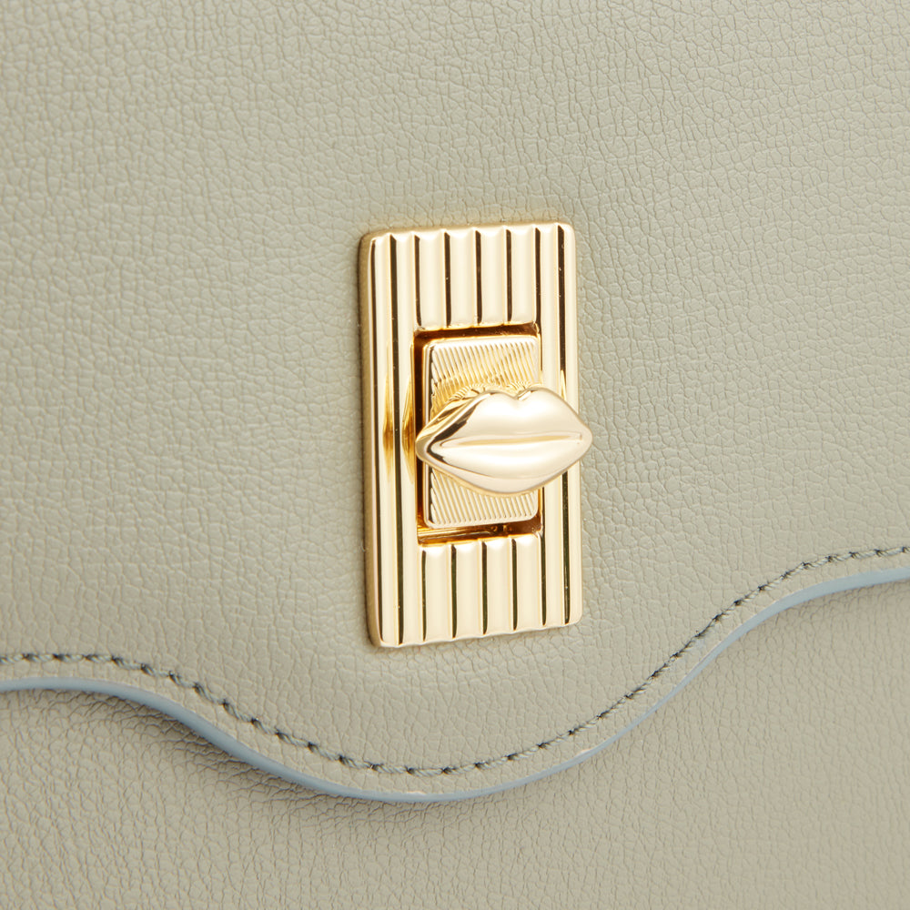 Close-up of a light sage green handbag's clasp; the clasp is gold with a lip-shaped detail.
