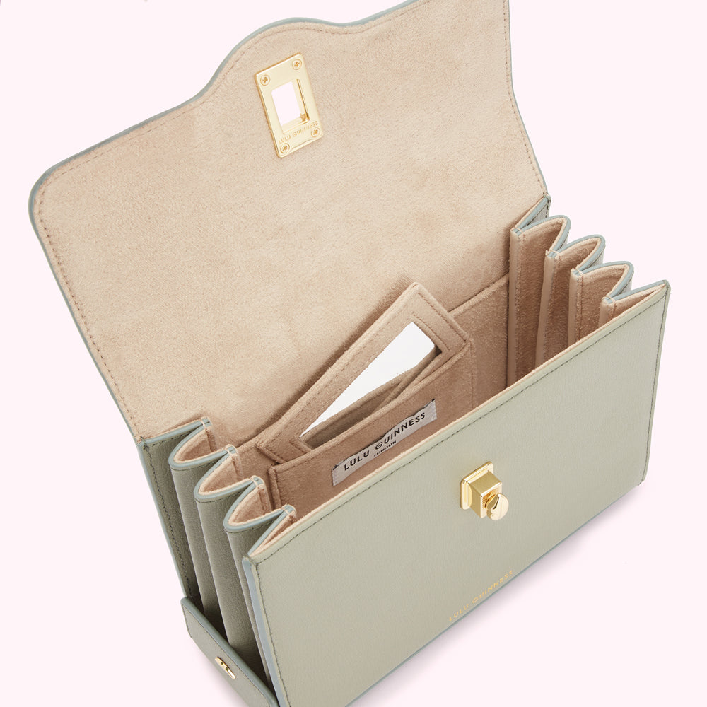 Sage green Lulu Guinness handbag opened to reveal beige interior with multiple compartments and a small mirror.