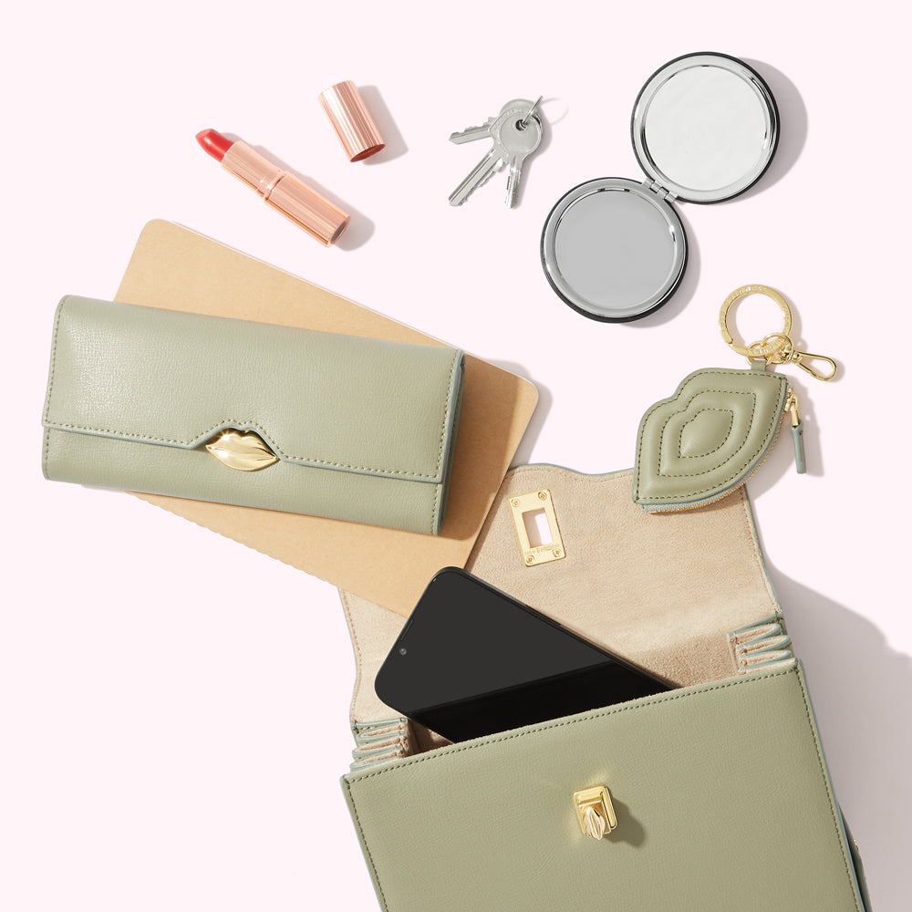 Sage green purse contents including a wallet, phone, lipstick, compact mirror, and keys.
