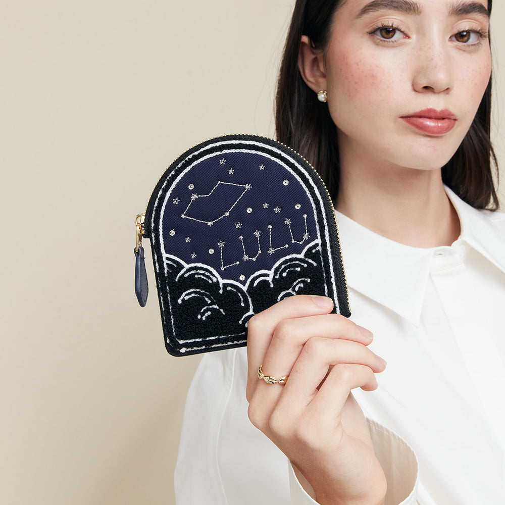 Woman holding a navy blue coin purse with star design and 'Lulu' branding.