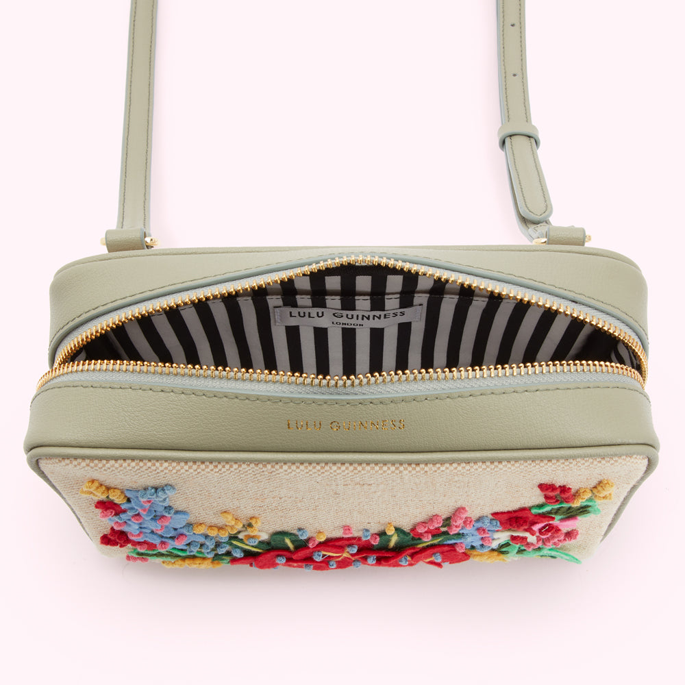 Sage green crossbody bag with embroidered flowers and a black and white striped interior. The bag is open to show the interior lining and gold Lulu Guinness logo.
