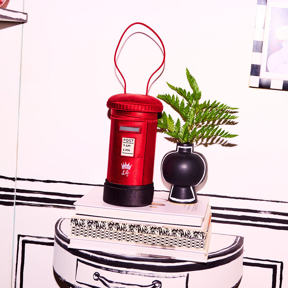 A red satin postbox shaped bag sitting on pile of books on a black and white side table.