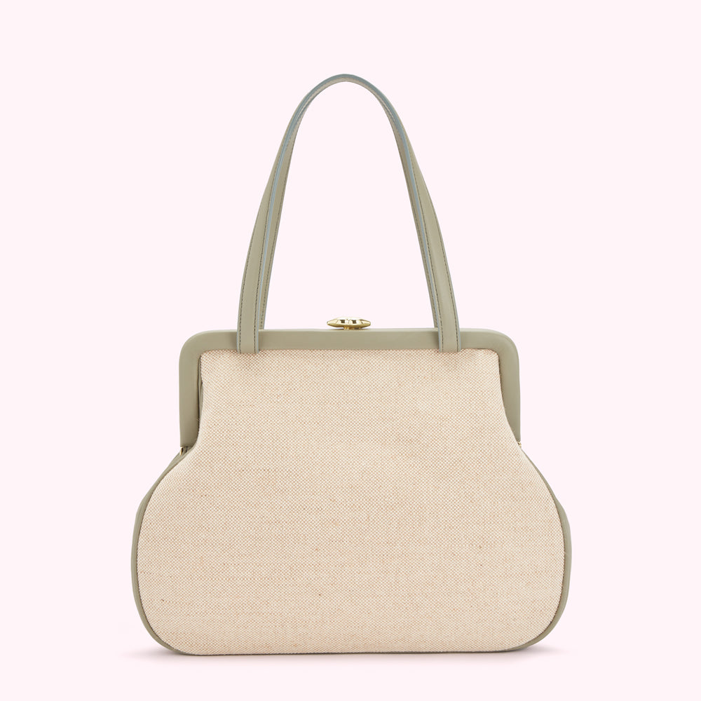 Beige canvas handbag with sage green leather trim and gold clasp against a white background.
