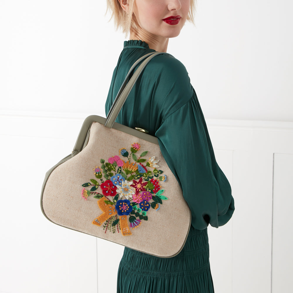 A woman in a green dress carries a beige handbag embroidered with a colourful bouquet of flowers.