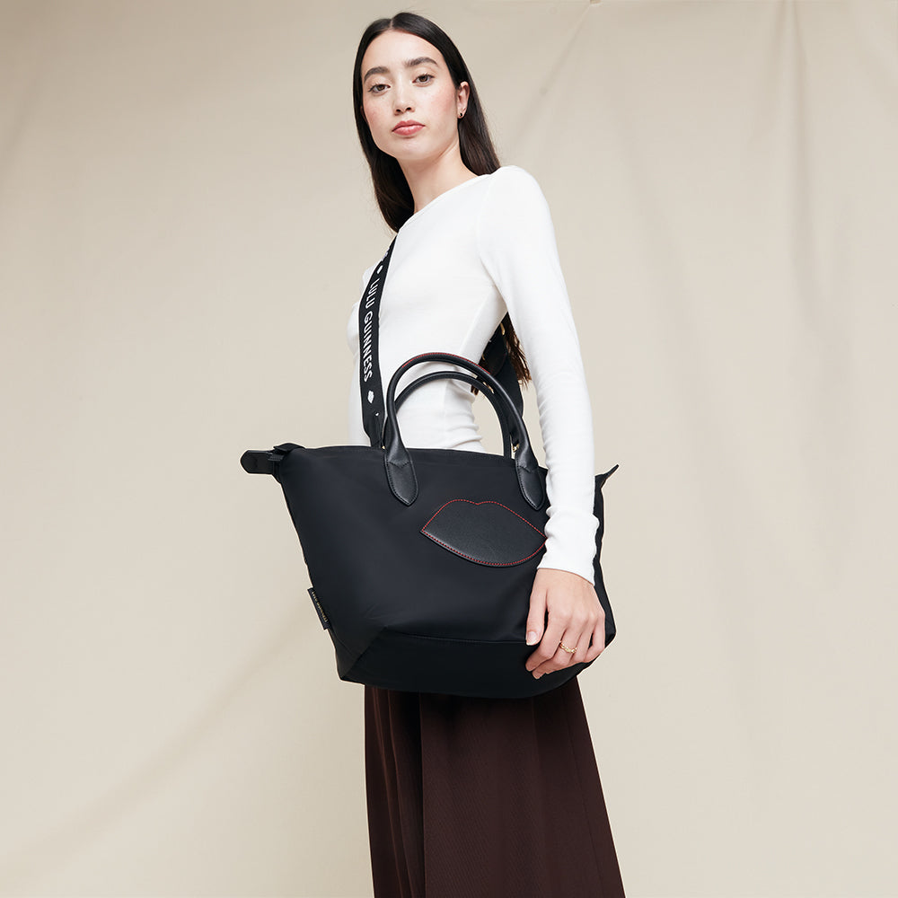 Woman holding a black nylon tote bag with detachable strap against a plain background