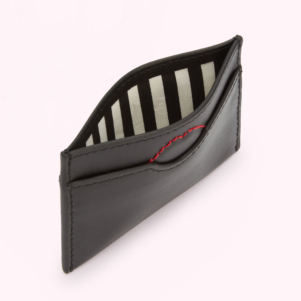 Black leather cardholder open to reveal a black and white striped interior with red stitching.
