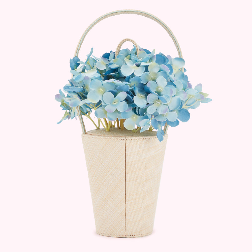 A bouquet of light blue hydrangeas on a beige woven handbag.
