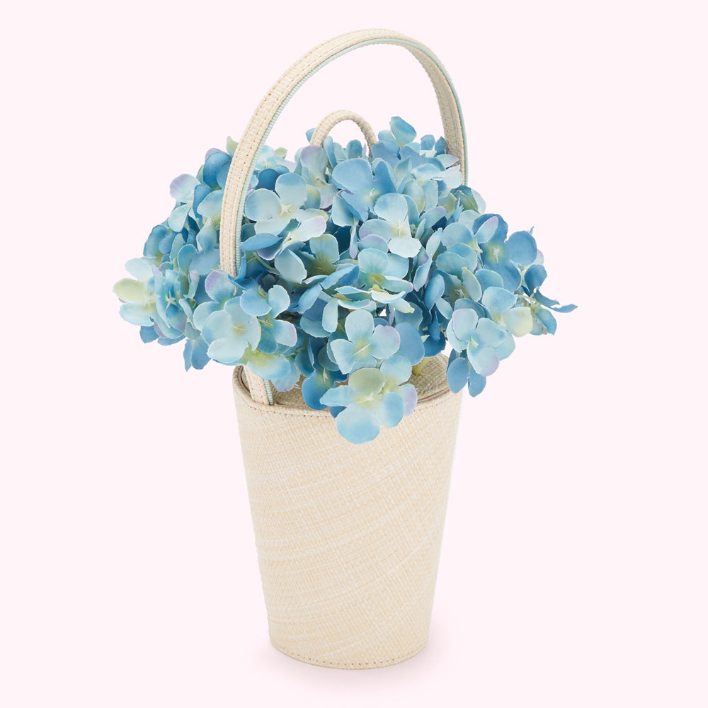 A bouquet of light blue hydrangeas in a cream-colored woven handbag.
