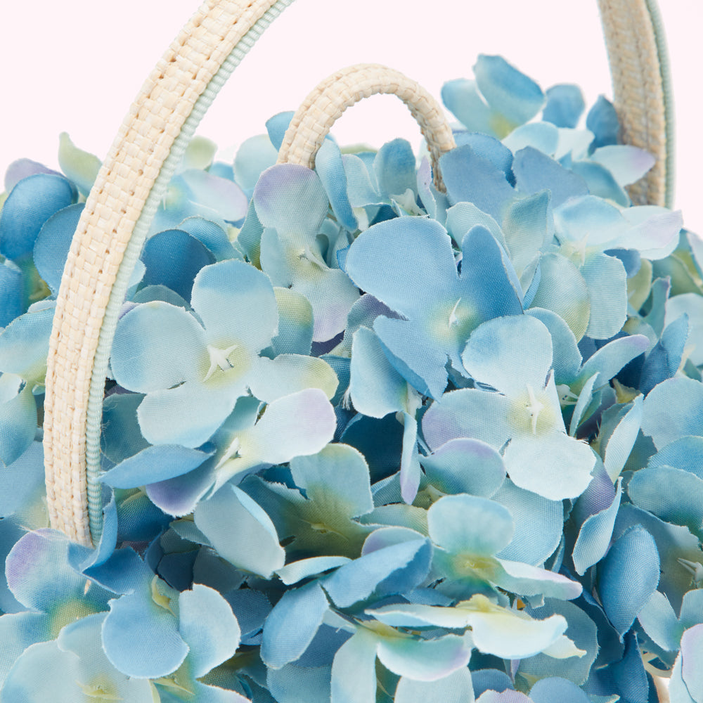 Close-up of a light blue fabric hydrangea arrangement in a light beige woven basket.
