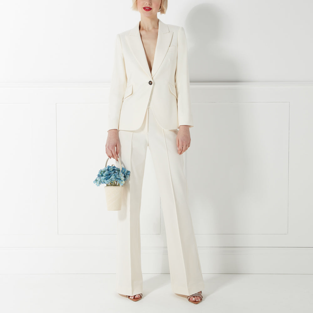 Woman in a white pantsuit holding a small bucket of blue flowers.
