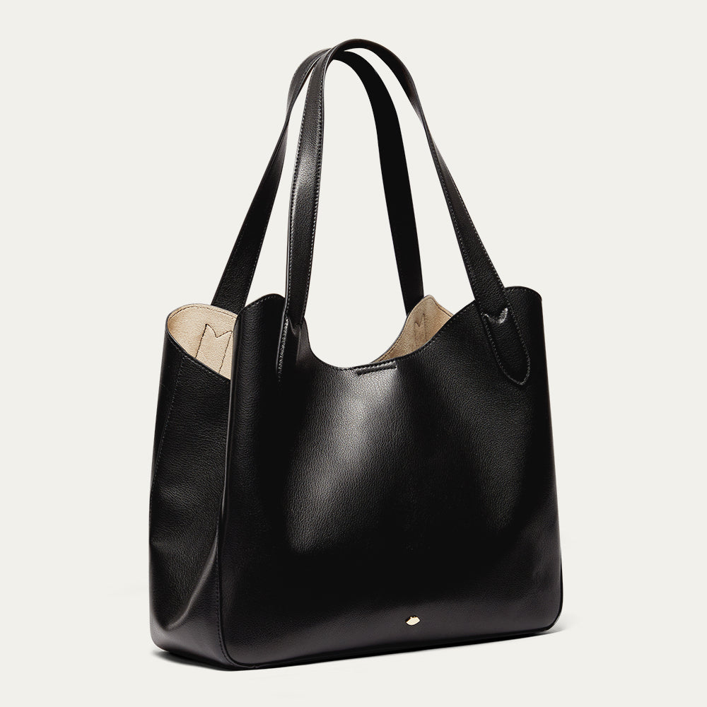 Black leather tote bag with a beige interior on a light grey background