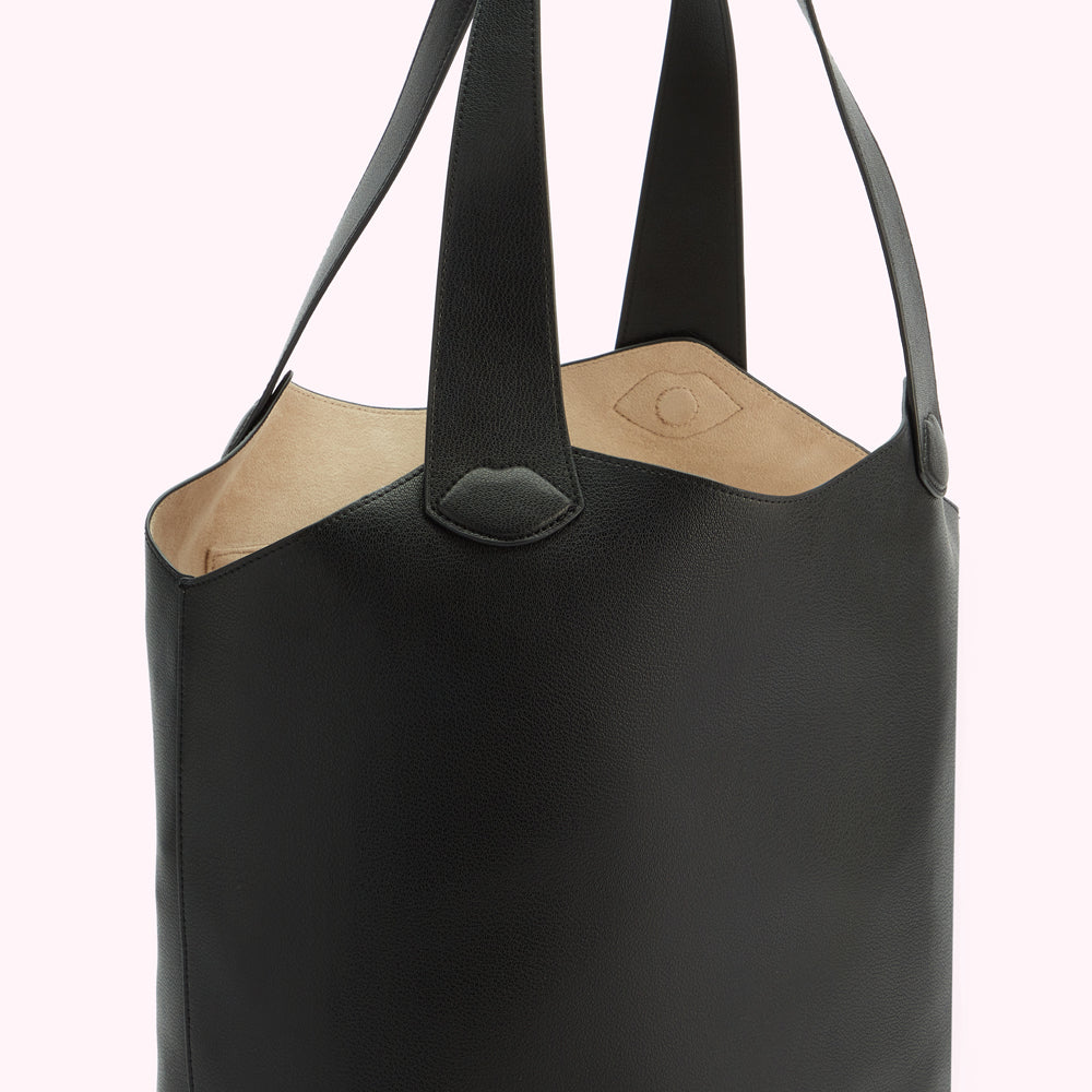 Close-up of a black leather tote bag with beige interior and leather handles.
