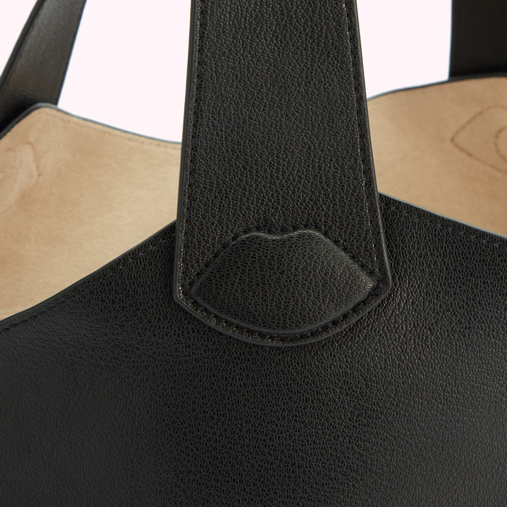 Close-up of a black leather handbag's handle, showing textured detail and a subtle lip-shaped design element.
