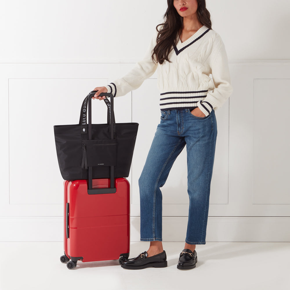 Model standing next to a red suitcase with a black nylon tote bag slotted over the suitcase handle.