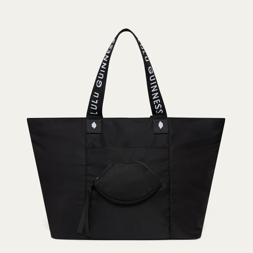 Black tote bag with Lulu Guinness handles and a lip-shaped pocket on a light grey background