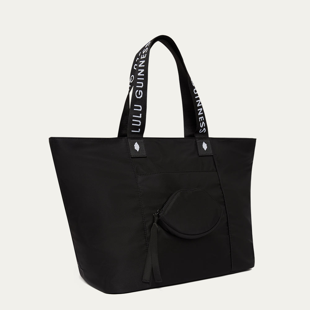 Black tote bag with Lulu Guinness logo on handle and a lip-shaped pocket on the front against a white background
