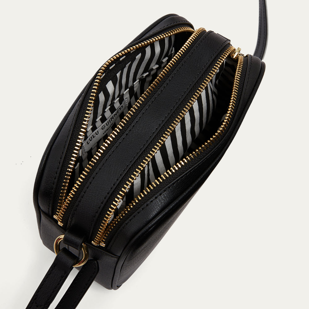 Black handbag with gold zippers open to reveal a black and white striped lining on a light grey background
