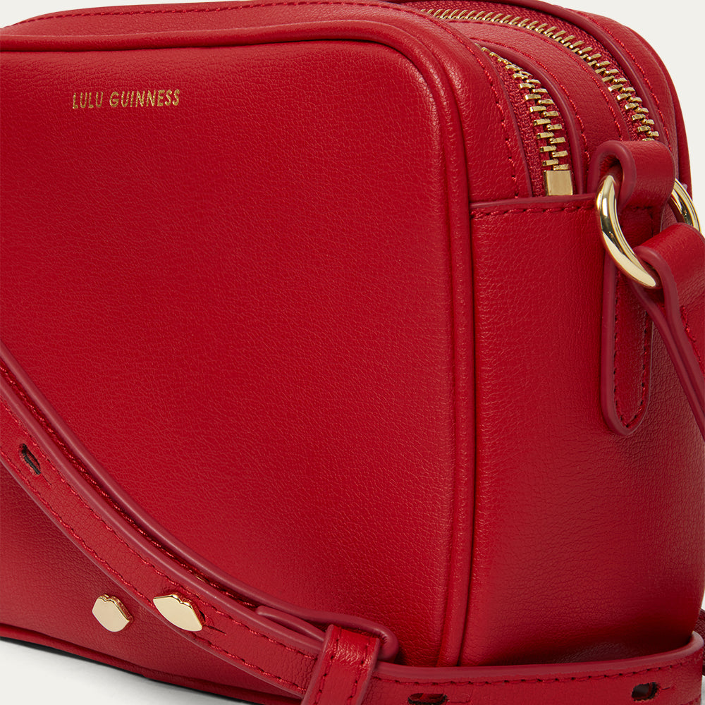 Red handbag with gold accents and 'Lulu Guinness' branding on a light grey background