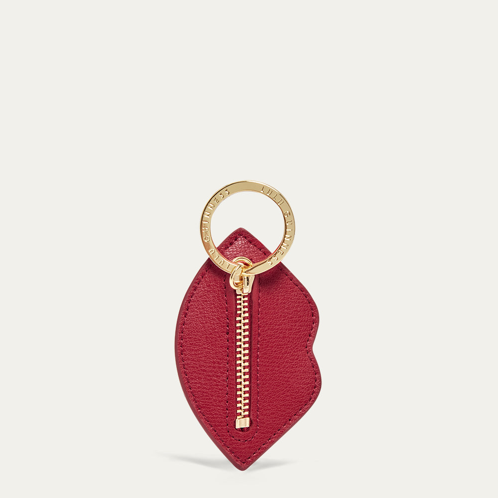 Red leather lip shaped keychain with gold zipper and ring on a light grey background