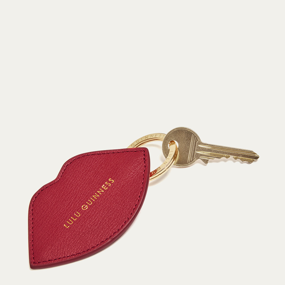 Red lip shaped keychain with a gold key and gold 'Lulu Guinness' logo on a light grey background