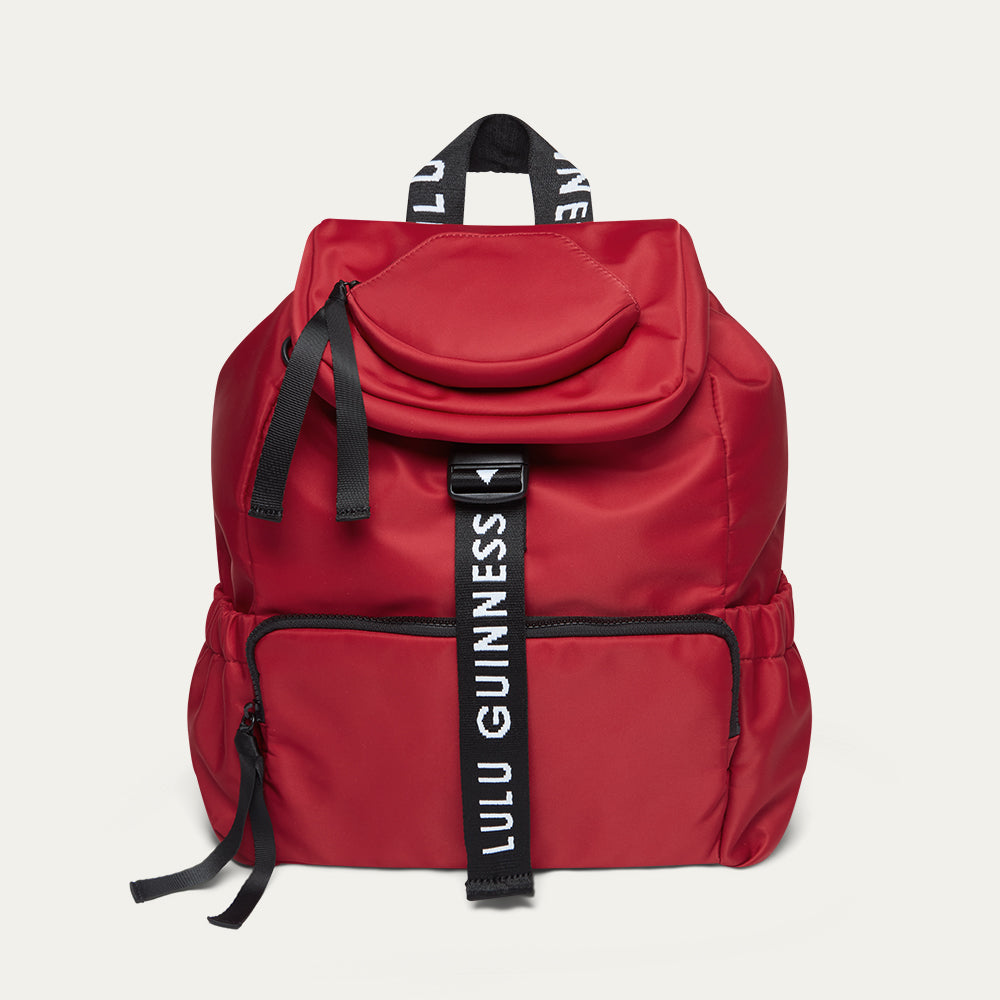 Red backpack with black straps and 'Lulu Guinness' branding on a white background