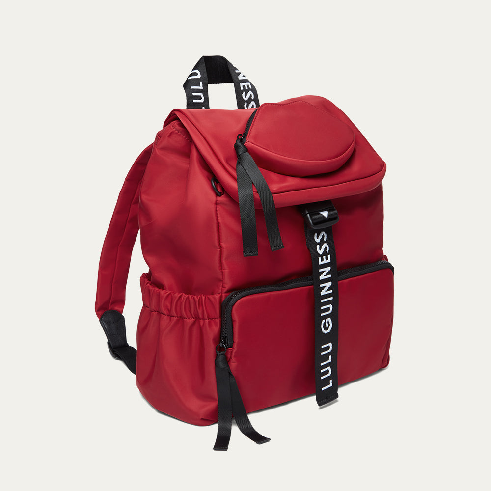 Red backpack with black straps and 'Lulu Guinness' branding on a light grey background