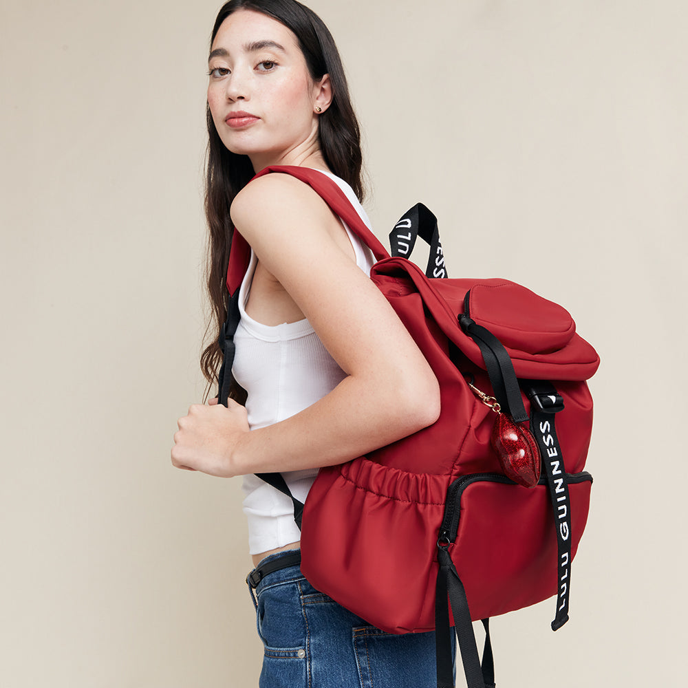 Woman wearing a red backpack with  'Lulu Guinness' branding on a beige background