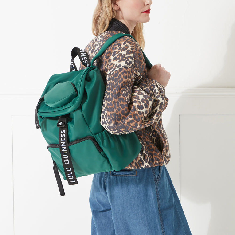 Model in a leopard print jacket, denim dress and red lipstick wearing a green nylon shoulder bag with branded 'Lulu Guinness' shoulder strap.