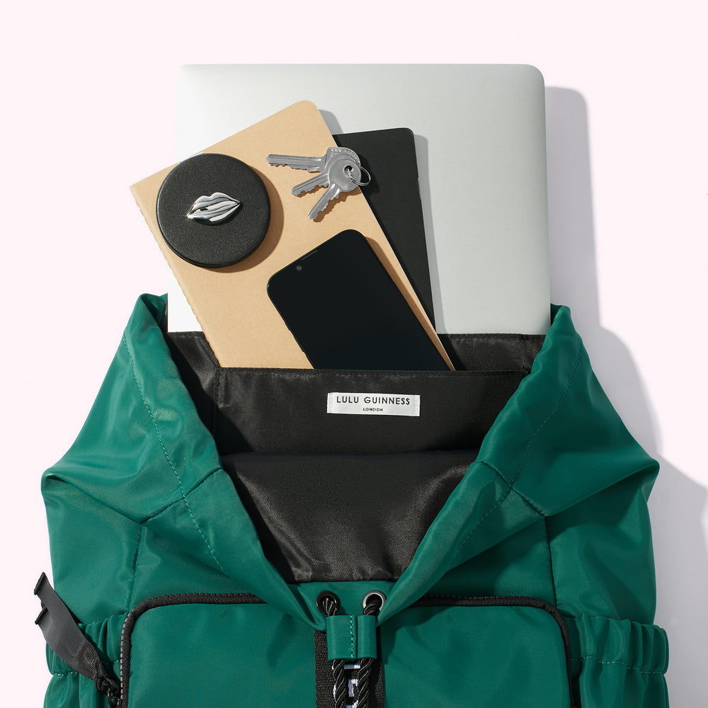 A Green nylon backpack with a laptop, notebooks, smartphone, keys and compact mirror spilling out.